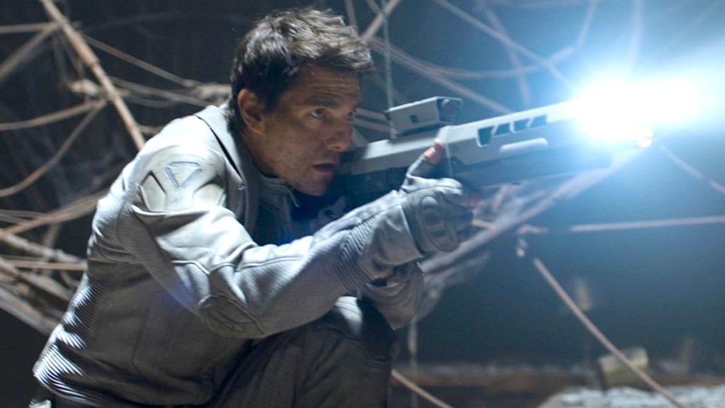 Tom Cruise en costume gris et gants, visant avec un fusil dans Oblivion