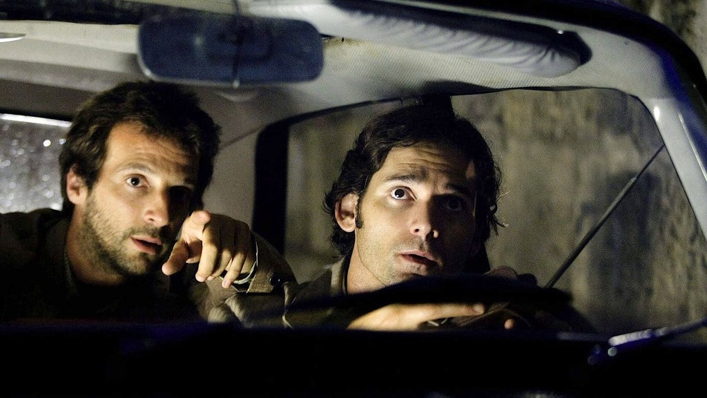 Mathieu Kassovitz et Eric Bana assis dans une voiture sombre dans Munich.